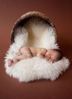 a newborn baby is sleeping in a basket on a brown background with fluffy white fur