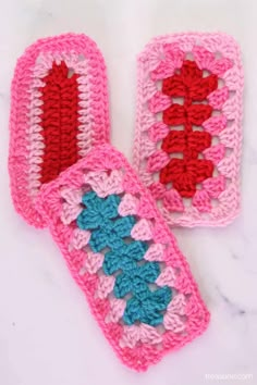 two crocheted pink and blue mitts on a white counter top, one has a red heart in the middle