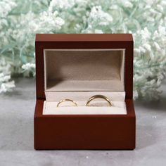 two wedding rings in a wooden box with white flowers behind them on a table top