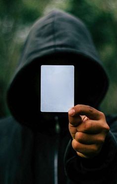 a person wearing a hooded jacket holding up a white card in front of their face