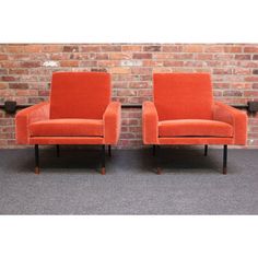 two orange chairs sitting next to each other in front of a brick wall