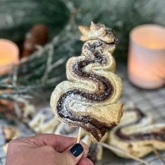 a hand holding a pastry on a stick in front of some candles and pine cones