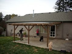 two dogs and three people are outside in front of a house with a covered patio