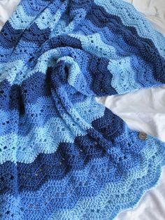 a blue crocheted blanket laying on top of a bed next to a pillow