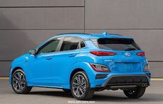 the rear end of a blue car parked in front of a gray wall with black rims