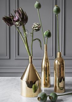 three gold vases with flowers in them on a marble countertop next to each other