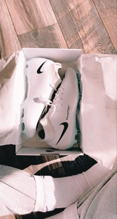 a pair of white nike shoes sitting in a box on top of a wooden floor