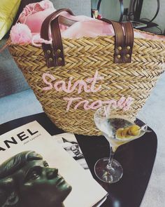 a table with a basket, magazine and wine glass on it next to a book