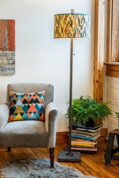 a living room with a chair, lamp and books on the floor