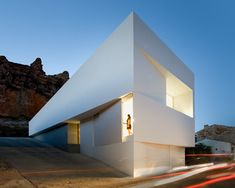 a white building sitting on the side of a road next to a mountain covered hillside