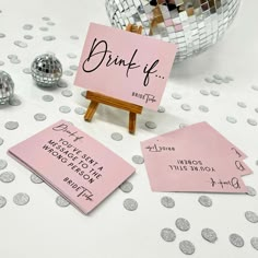 some pink signs and silver disco balls on a white table with confetti in the background