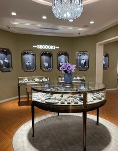 a glass table with plates on it in front of several framed pictures and a chandelier