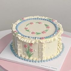 a decorated cake sitting on top of a pink tablecloth covered plate with white frosting