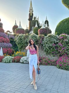 a woman in a pink top and white skirt is walking through the flower garden at disney world