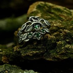 a silver ring with leaves and green stones on top of mossy rocks in the woods