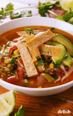 a bowl of mexican soup with tortilla chips and avocado on the side