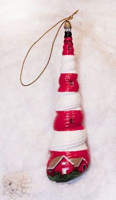 a red and white lighthouse ornament hanging from a gold chain on a white surface