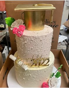 a three tiered white wedding cake with gold topper and pink flowers on the side