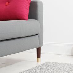 a grey couch with red pillows and a rug on the floor in front of it