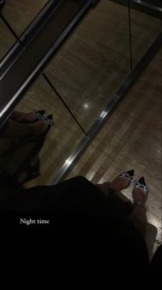 someone's feet on the ground in front of an escalator at night time