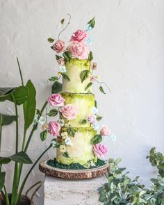 a three tiered cake with pink and green flowers on the top is surrounded by greenery