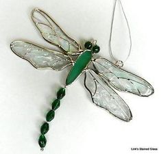 a green and white dragonfly ornament hanging from a chain on a white surface