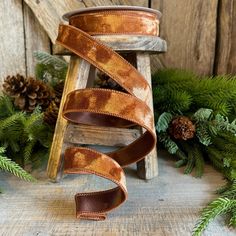 a roll of brown leather ribbon next to evergreen branches and pine cones