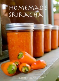 several jars of homemade sriraca sit on a window sill next to peppers