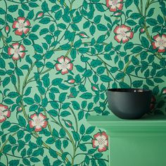 a green wall with pink flowers on it and a black bowl sitting on the side