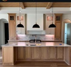 a large kitchen with wooden cabinets and black pendant lights hanging from the ceiling over the island