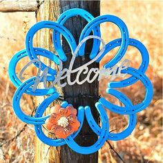 a welcome sign hanging on a fence post in the fall with an orange flower attached to it