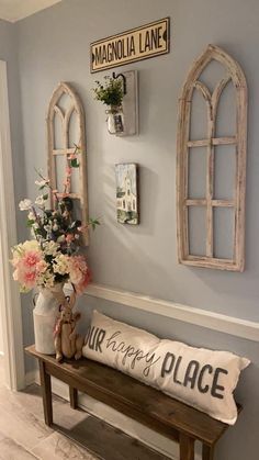 a wooden bench sitting in front of a wall with two windows and flowers on it