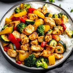 a white plate topped with chicken and veggies next to rice on top of a table