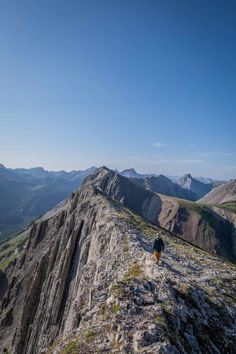 a person walking up the side of a mountain with mountains in the background and blue sky