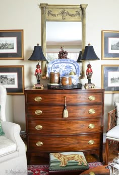 a dresser with two lamps and pictures on the wall behind it in a living room