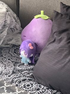 a purple stuffed animal next to two pillows on a bed with black and white sheets