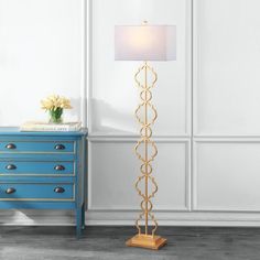 a gold floor lamp with a white shade on it and a blue dresser in the background