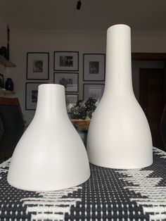 two white vases sitting on top of a black and white tablecloth covered table