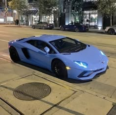 a blue sports car is parked on the side of the road at night in front of a building