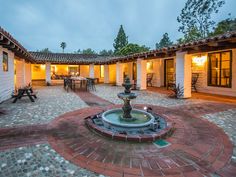 a courtyard with a fountain in the middle and tables around it at night, surrounded by brick pavers