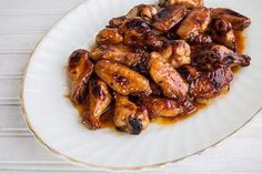 a white plate topped with chicken wings covered in sauce on top of a wooden table