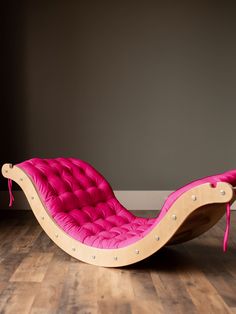 a pink chaise lounge chair sitting on top of a hard wood floor next to a gray wall