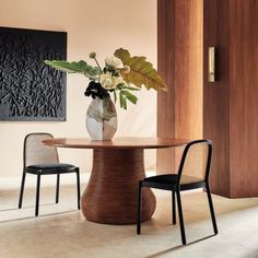 a vase with flowers sitting on top of a wooden table next to two black chairs