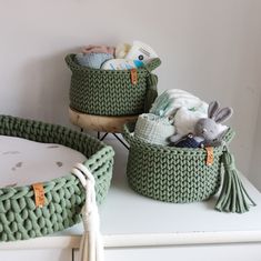 two baskets filled with baby items sitting on top of a white dresser next to a wall