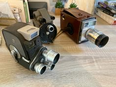 two old cameras sitting on top of a wooden table next to books and other items