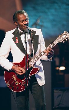 a man in a tuxedo singing into a microphone and playing an electric guitar