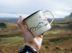 a hand holding a coffee cup with mountains in the background