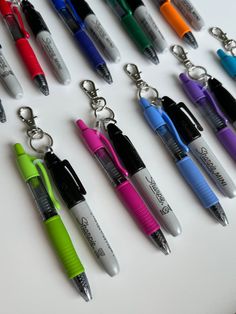 many different colored pens are lined up on a table next to each other and one has a keychain