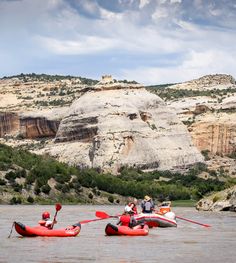 two people in red kayaks paddling on the water with cliffs in the background