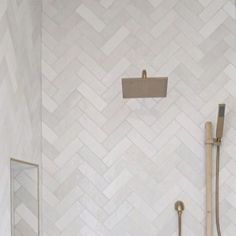 a white bathroom with herringbone tile on the wall and shower head in the corner